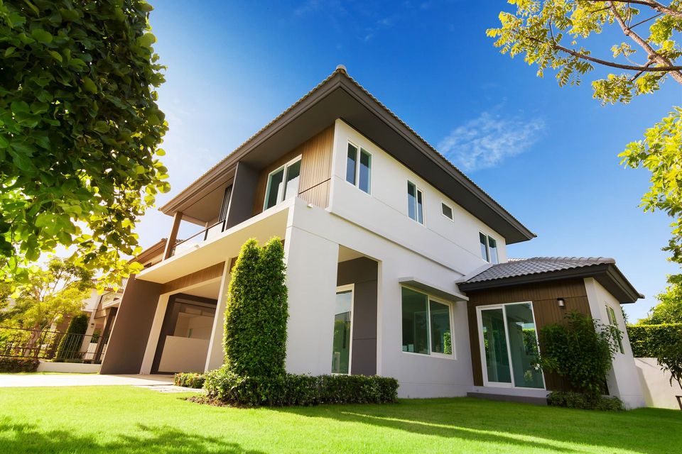 Modern two-story white house with green lawn and blue sky, framed by trees