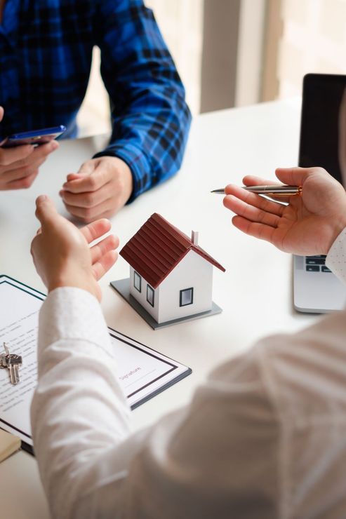 People discussing a small house model at a table during a meeting