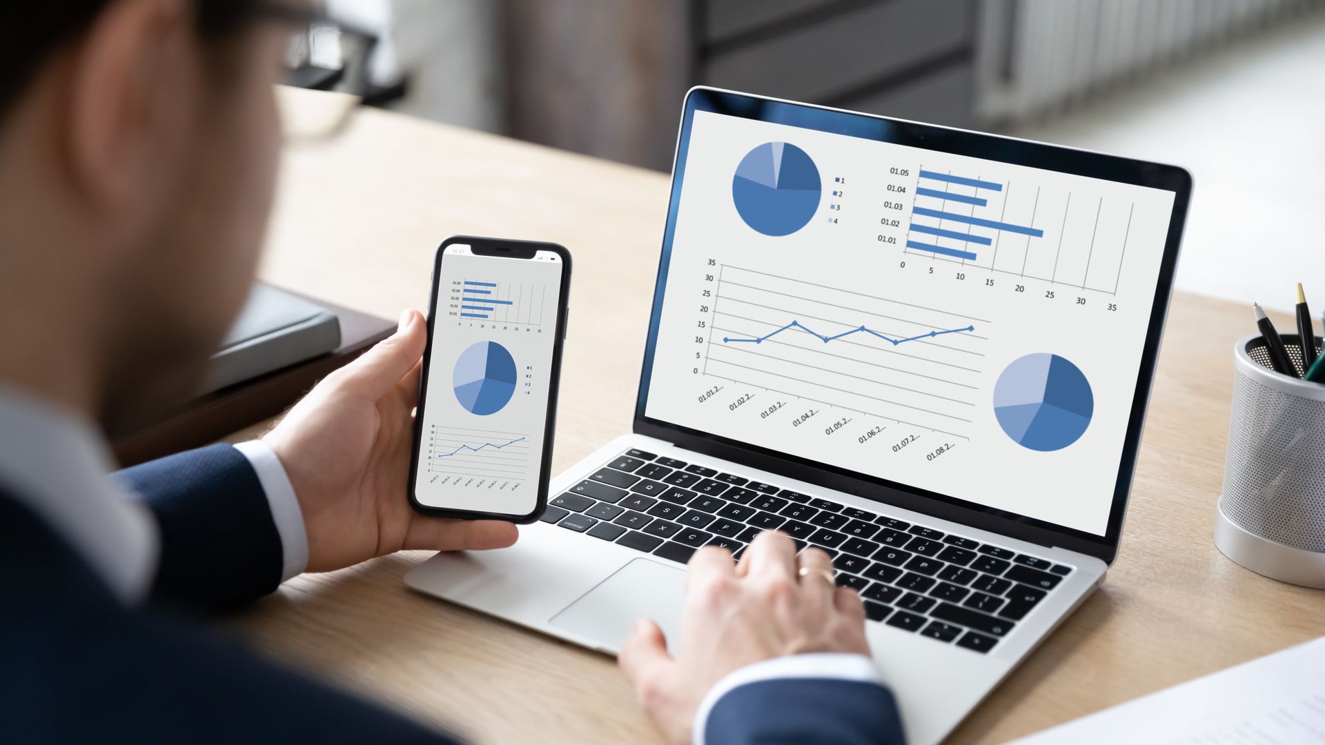 Person using a smartphone beside a laptop displaying business analytics charts.