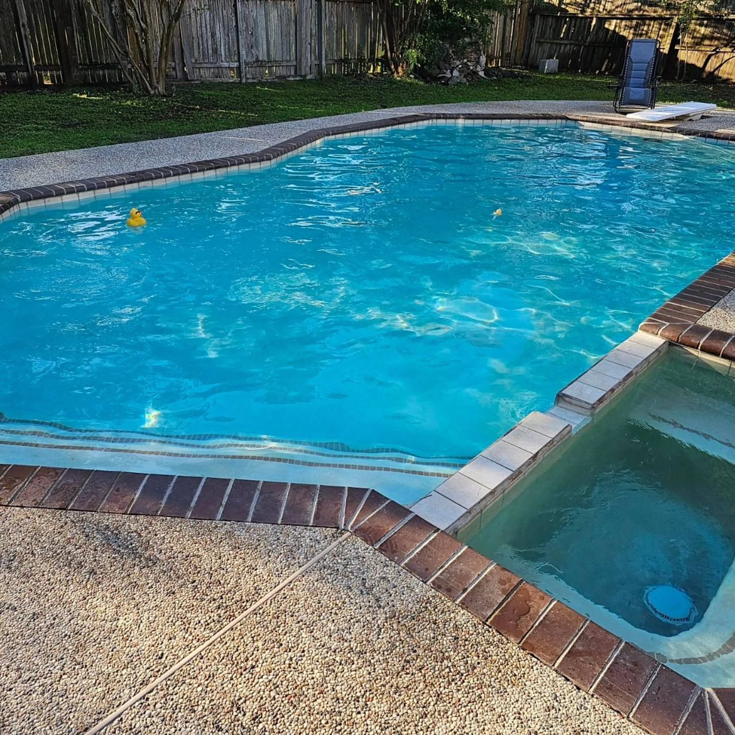 Backyard swimming pool with blue water and attached hot tub, bordered by brick and stone decking.