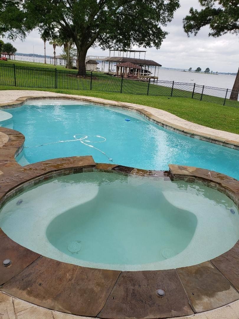 Small round hot tub beside a bright blue pool, with trees and a lakeside lawn in the background