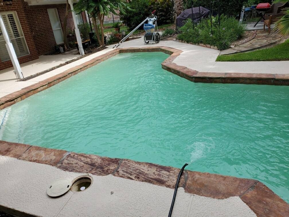 Backyard swimming pool with turquoise water, stone coping, and lounge chairs beside a patio.