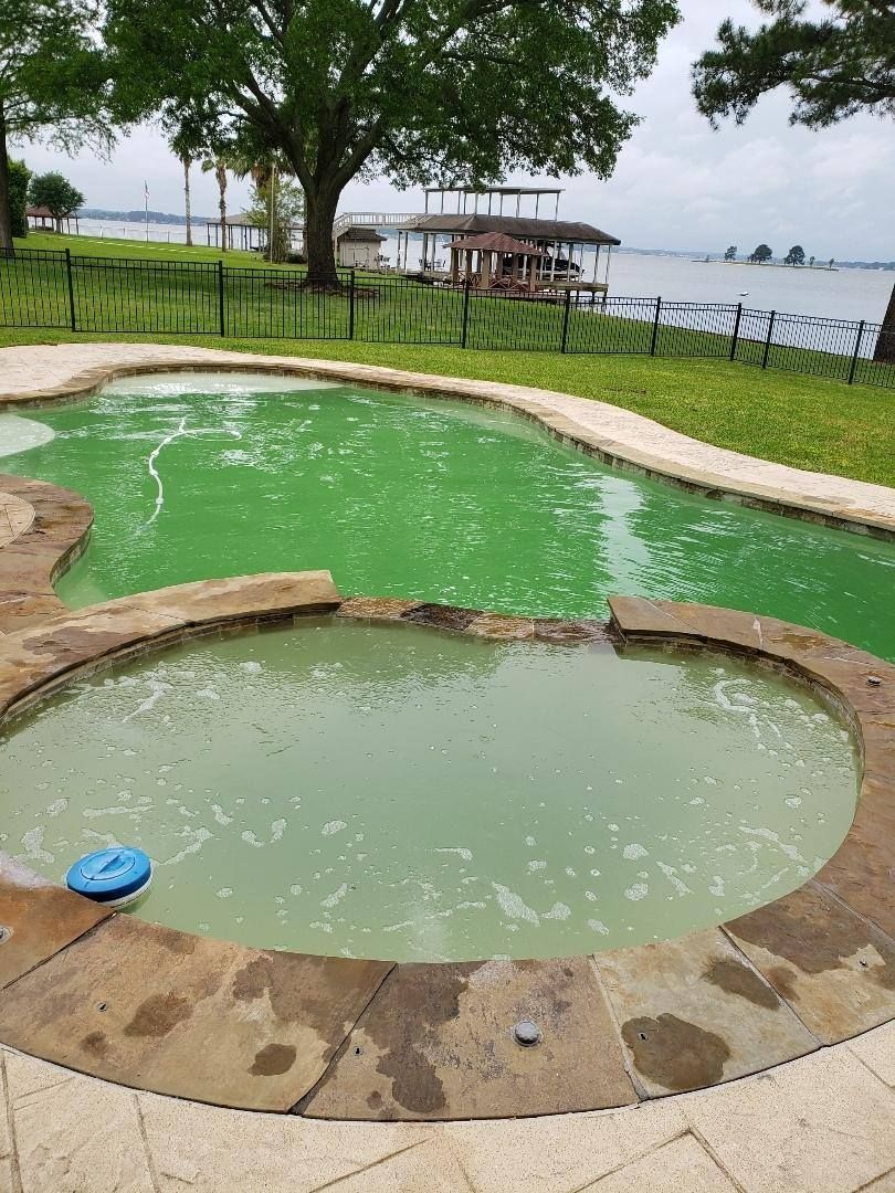 Two small green pools by a lakeside lawn with trees, rocks, and a wooden dock in the background