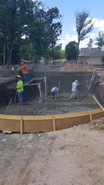 Workers pouring concrete for a curved backyard pool shell in a residential yard.