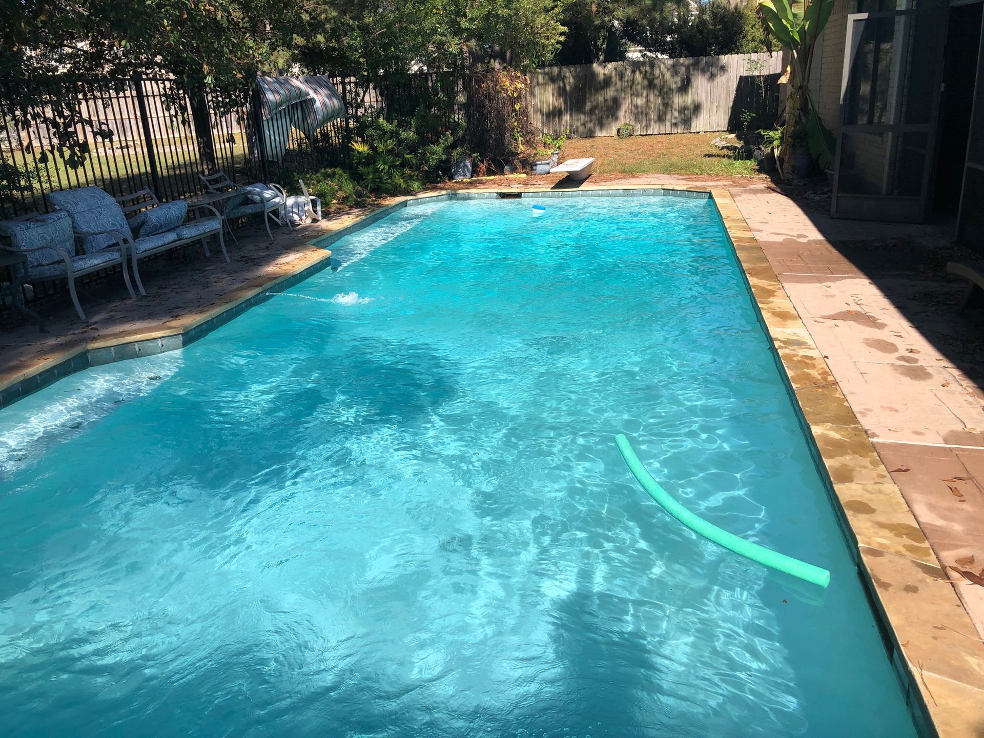 Backyard swimming pool with blue water, lounge chairs, and trees along the fence