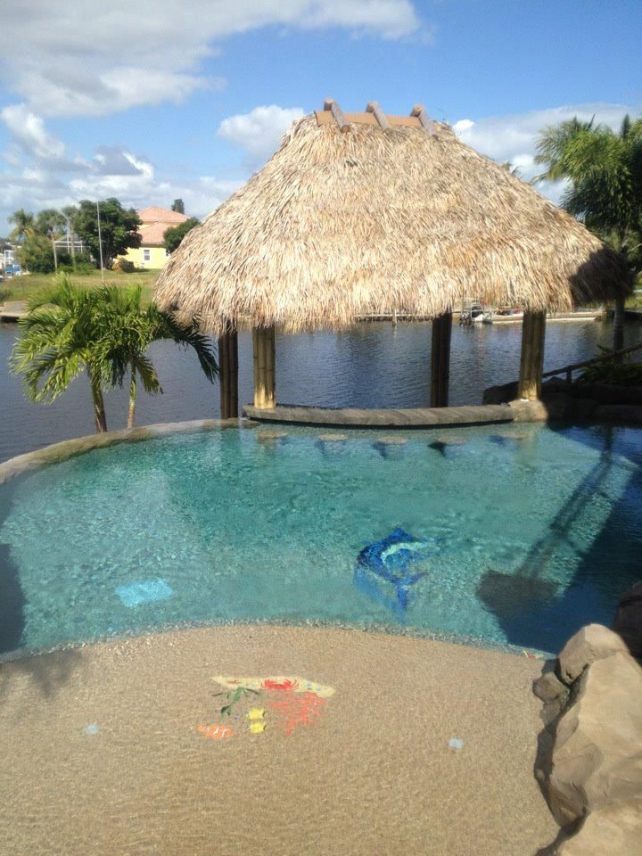 Tropical pool with thatched hut, blue water, and ocean view under a partly cloudy sky