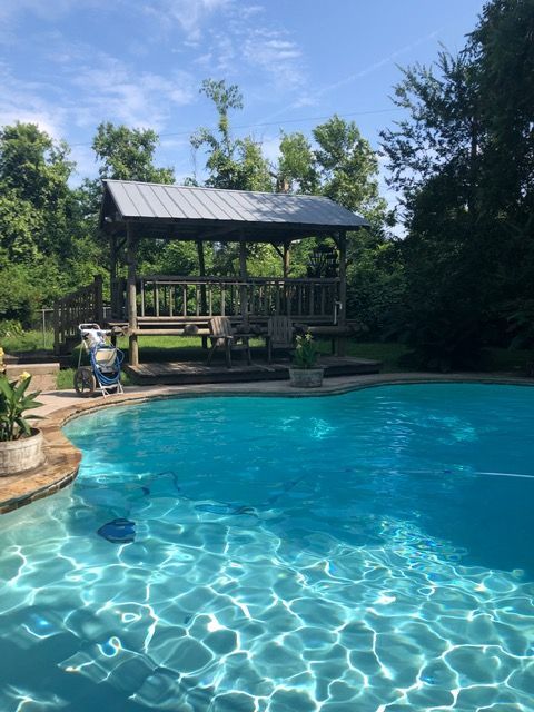 Backyard pool with sparkling blue water and a covered pavilion surrounded by trees