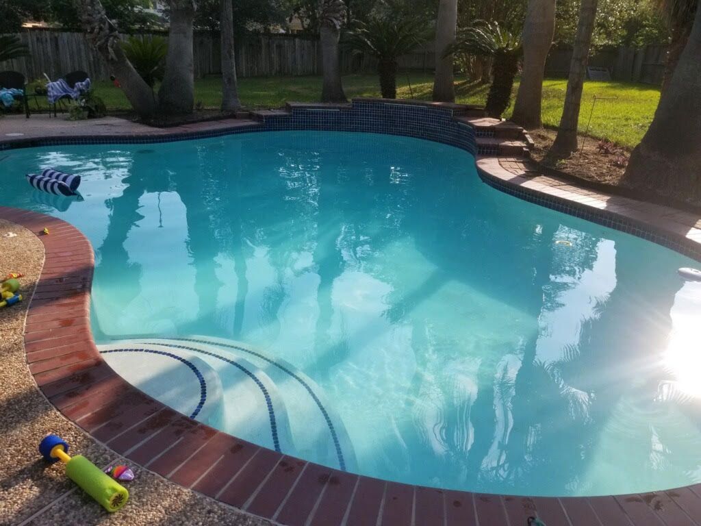 Backyard swimming pool with turquoise water, brick coping, and a green toy by the steps
