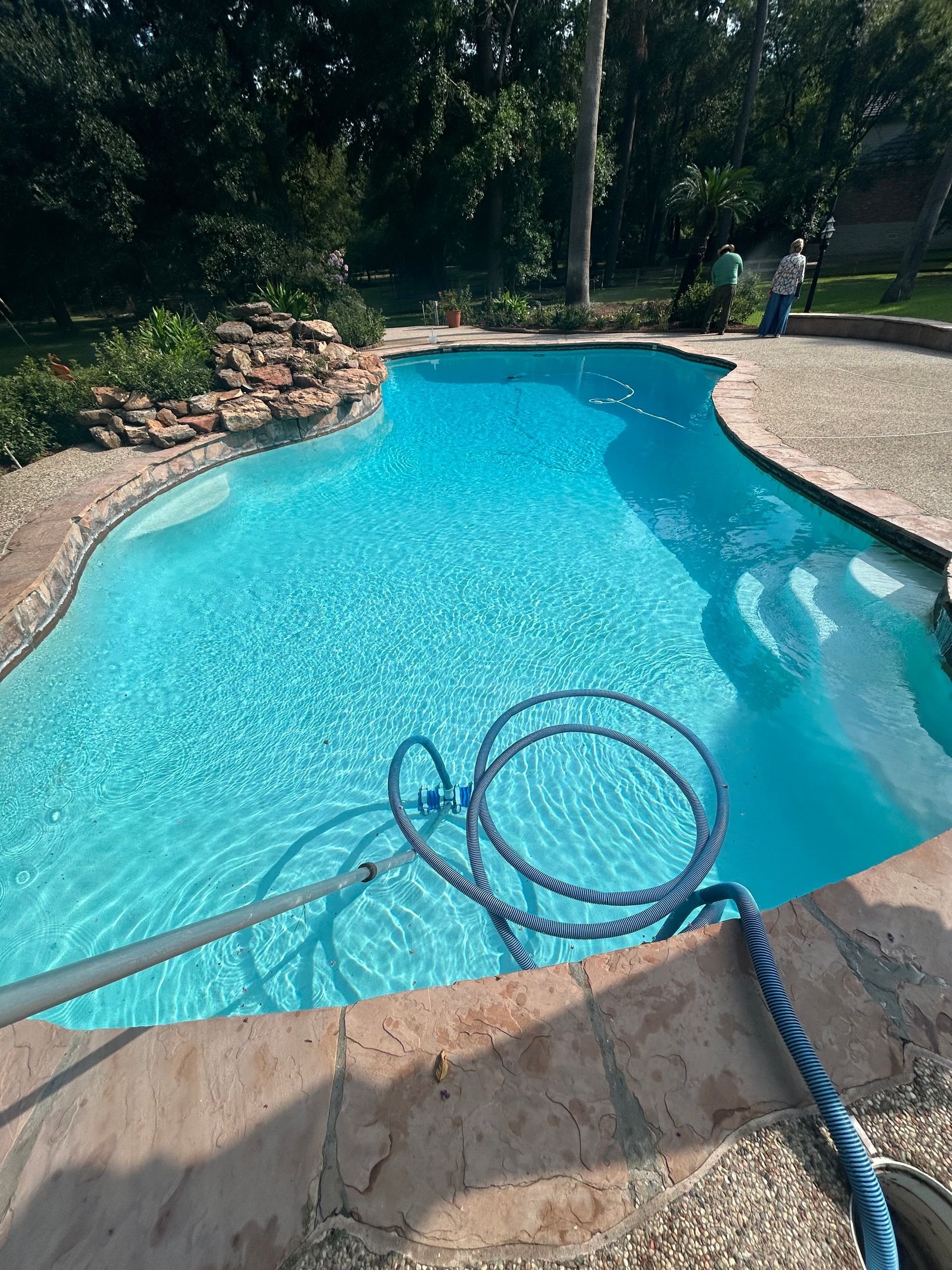 Blue swimming pool with rope handrail, stone deck, and trees in the background