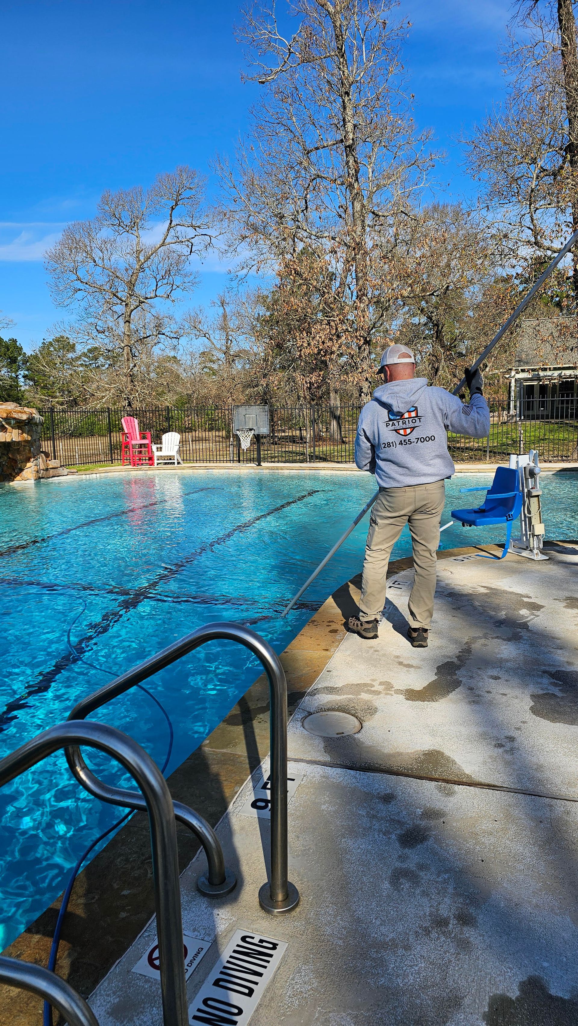 Person standing beside a turquoise swimming pool on a sunny day with trees and loungers in the background