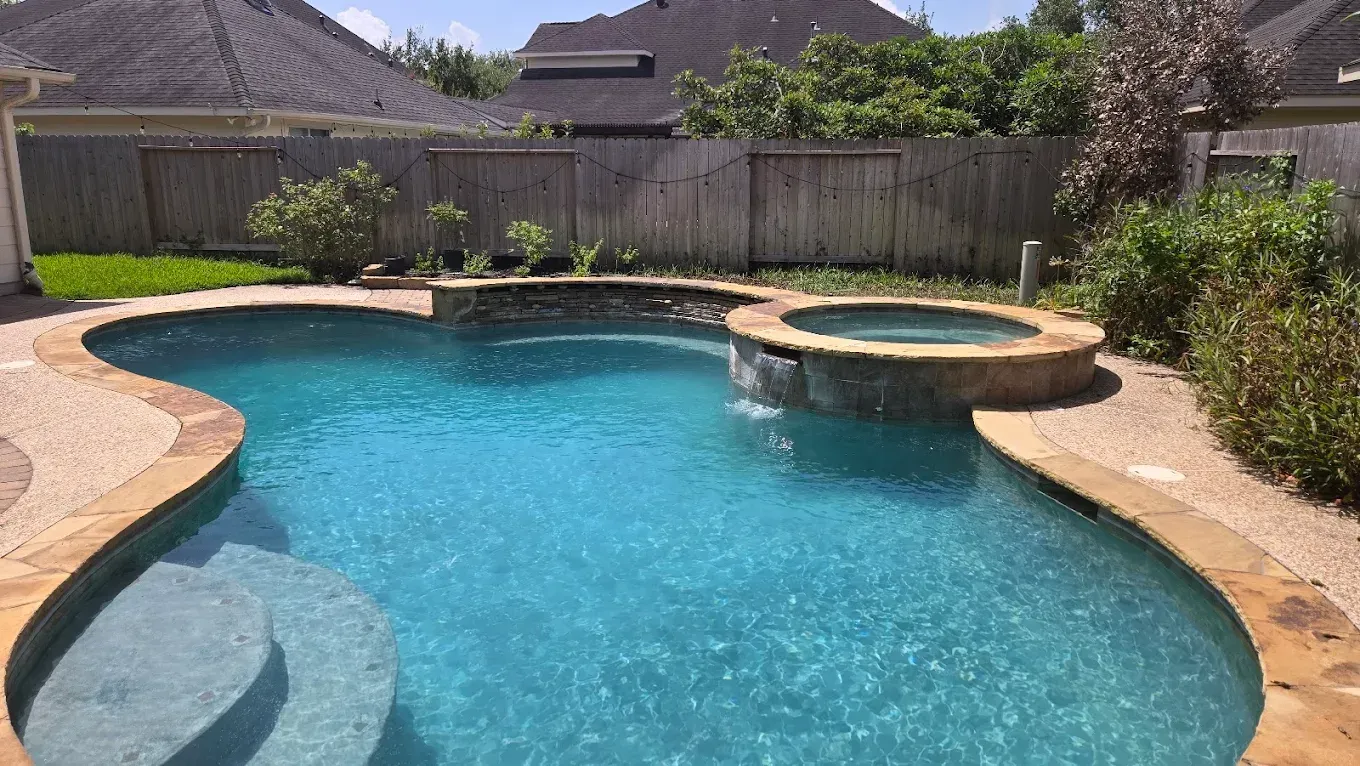 Backyard swimming pool with blue water, stone coping, and a raised circular spa