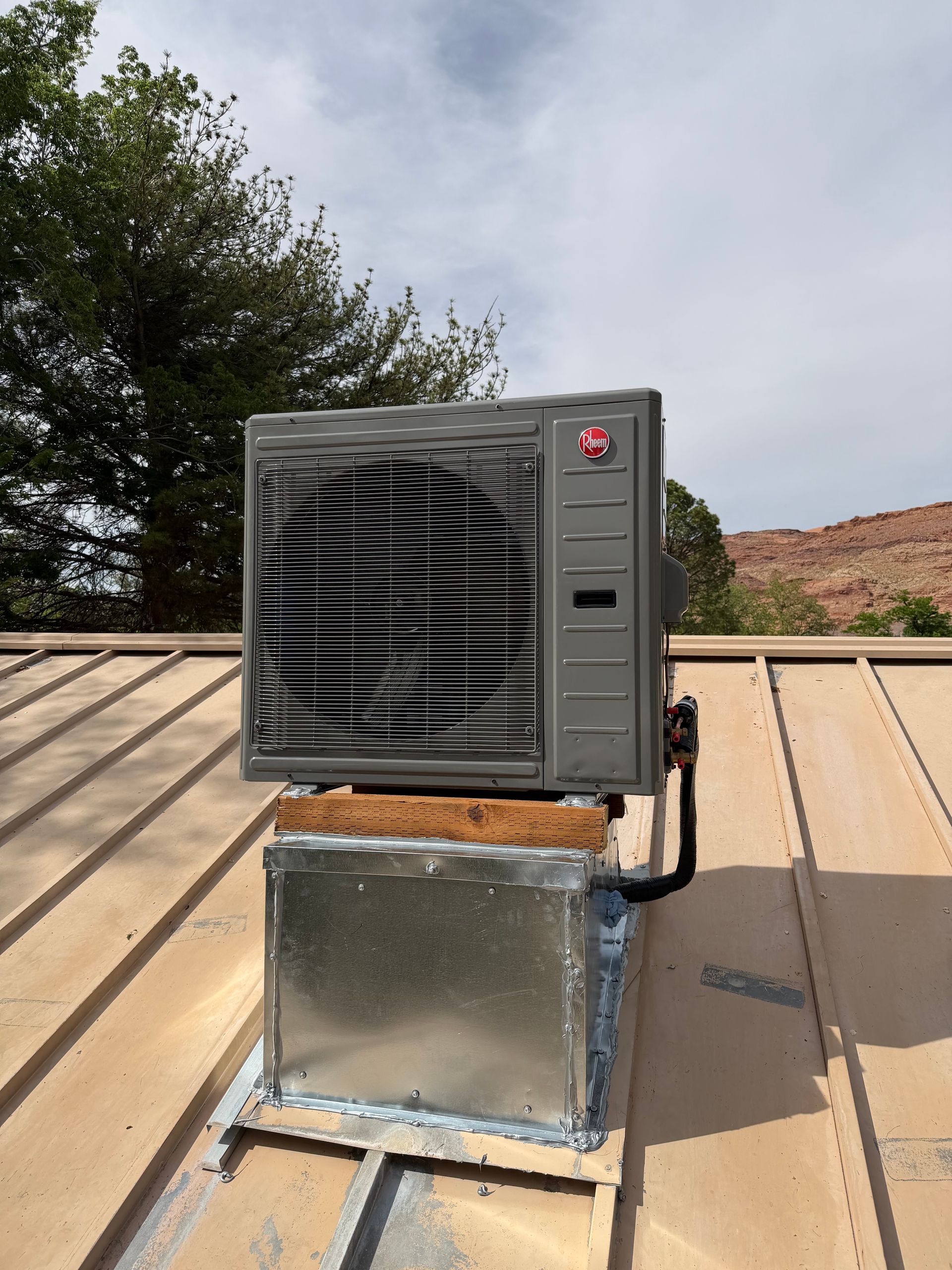 Outdoor HVAC unit mounted on a roof beside a metal duct enclosure under a cloudy sky