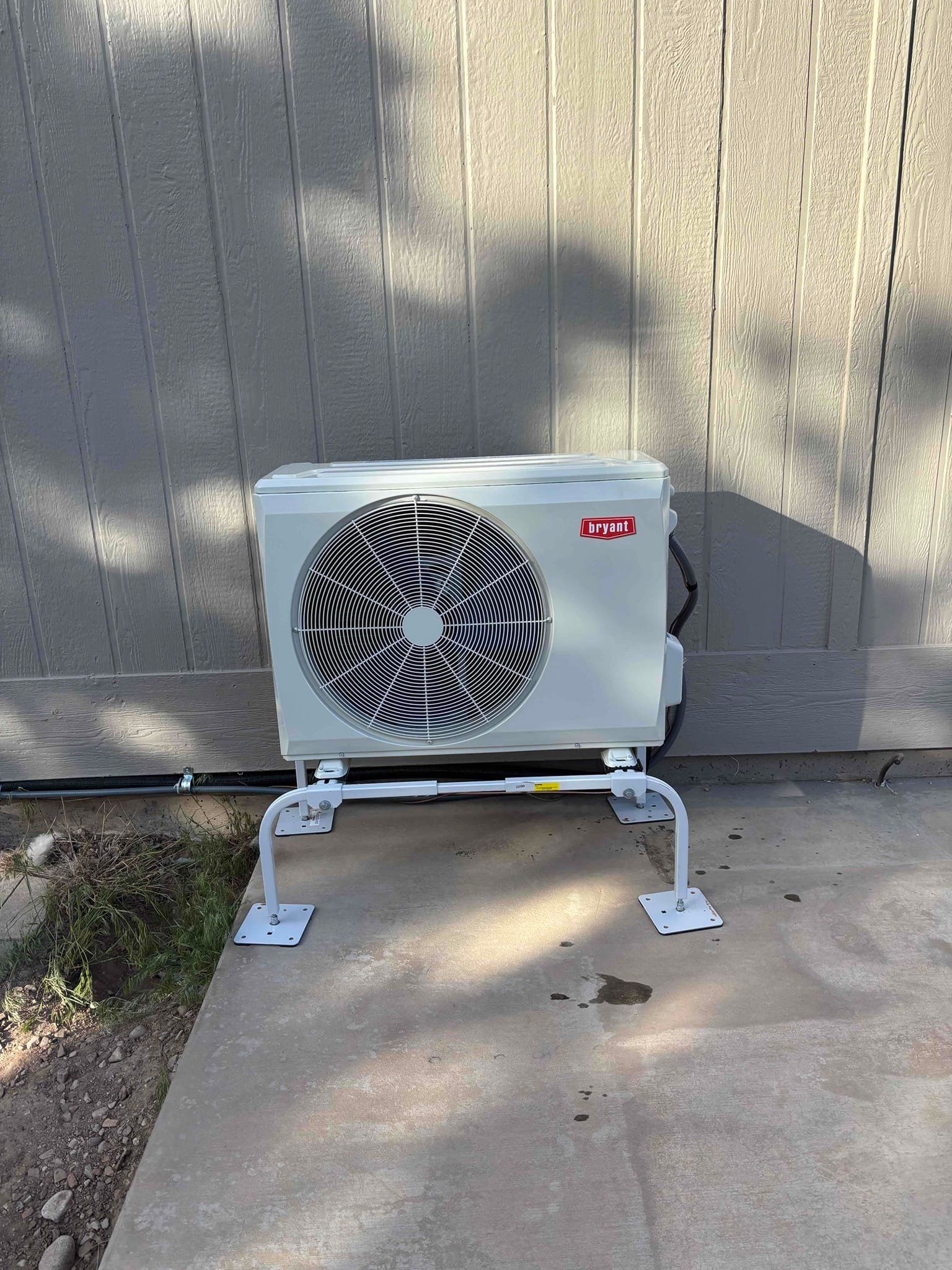 Outdoor AC unit on white metal stand against a beige wall, with a large black-and-white fan cover.