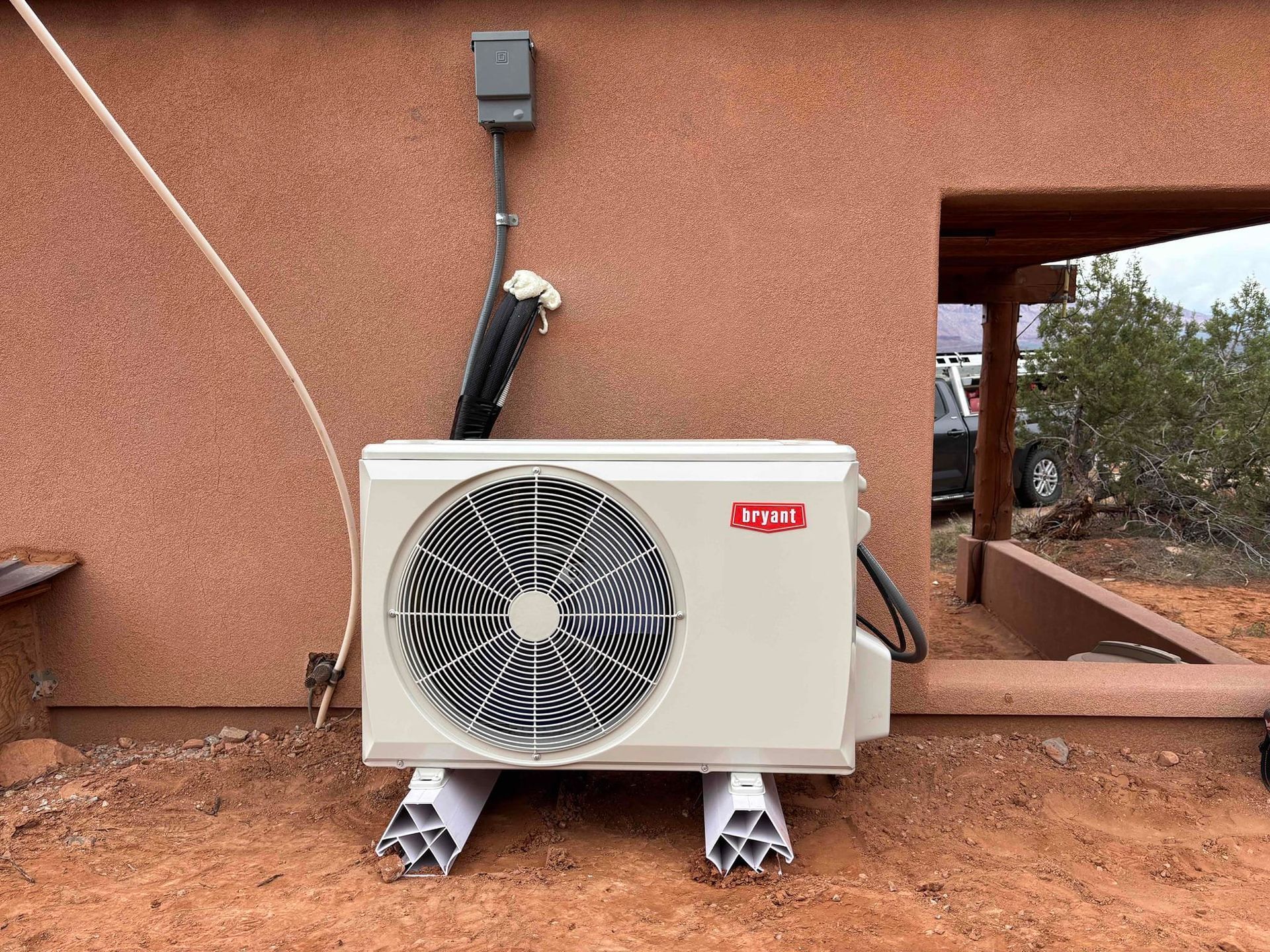Outdoor air-conditioning unit against a stucco wall with a visible drain hose and electrical box