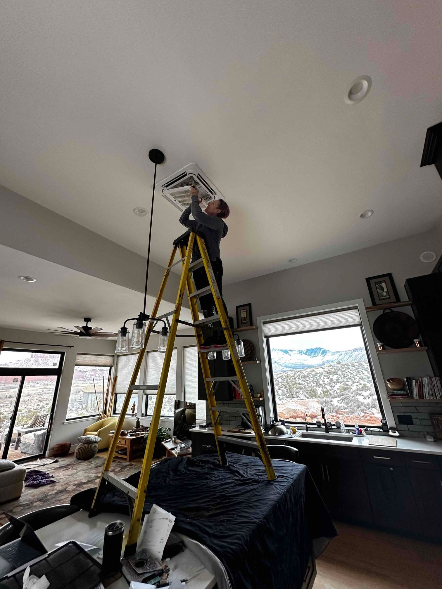Person on a yellow ladder installing a ceiling light in a bright living room