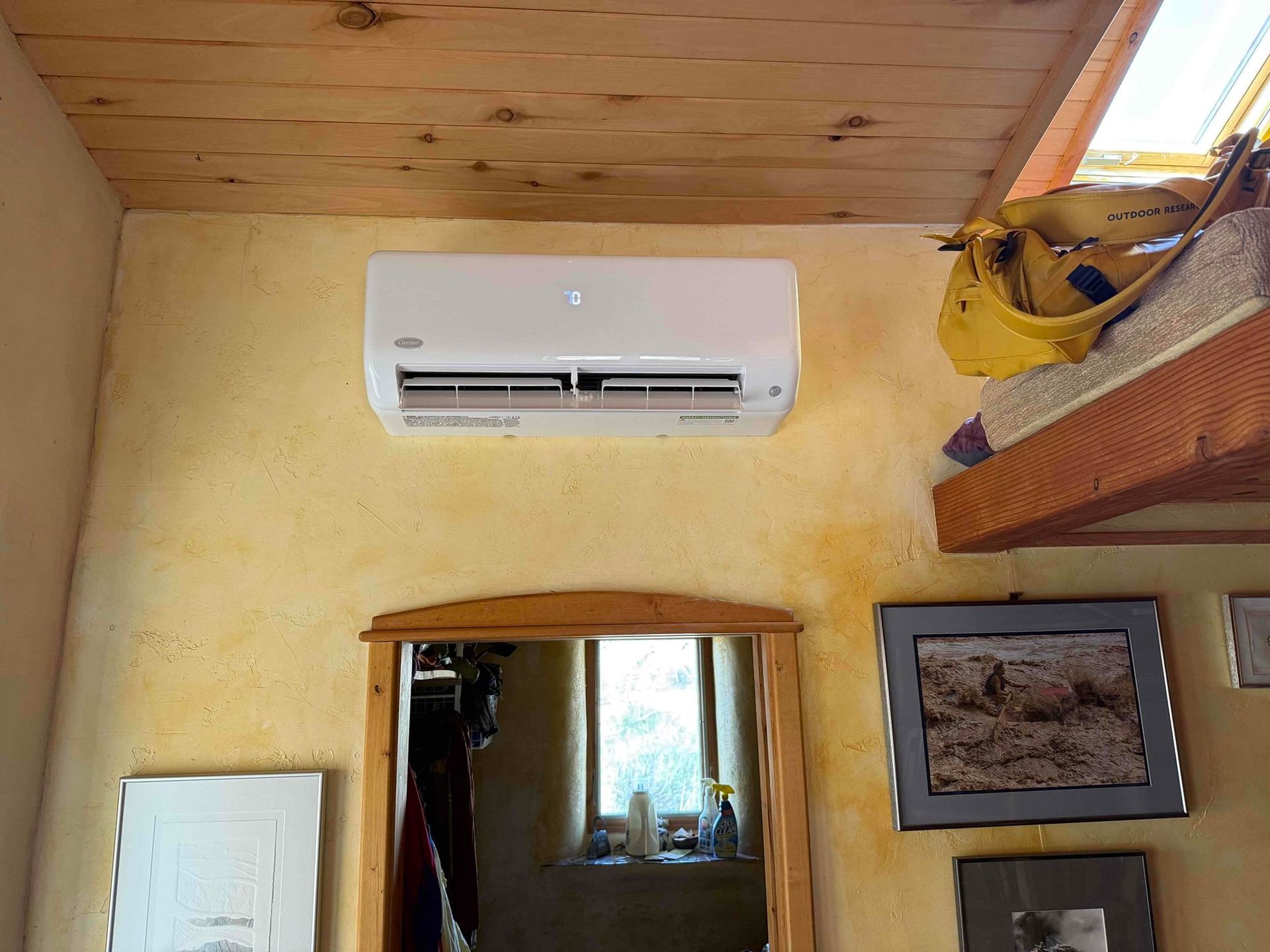 Wall-mounted white air conditioner above a doorway in a yellow room with a wooden ceiling.