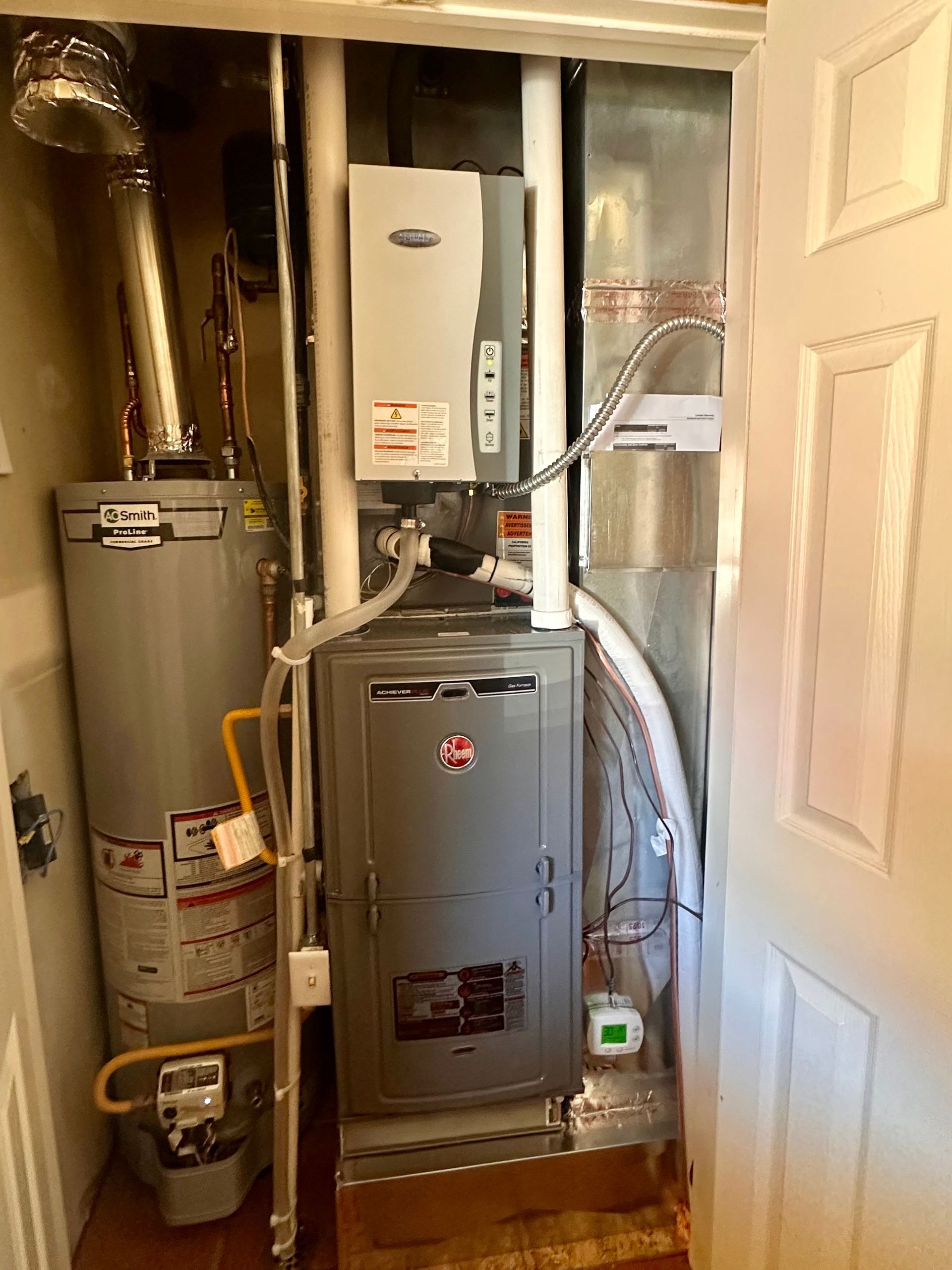 Open furnace and water heater in a narrow utility closet, with ducts and pipes visible.