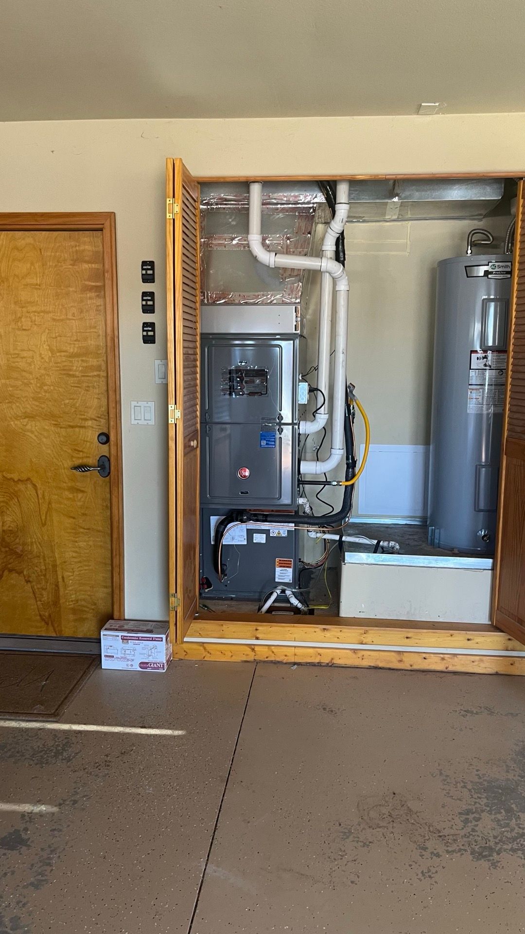 Open utility closet with furnace, water heater, and exposed ductwork next to a wooden door