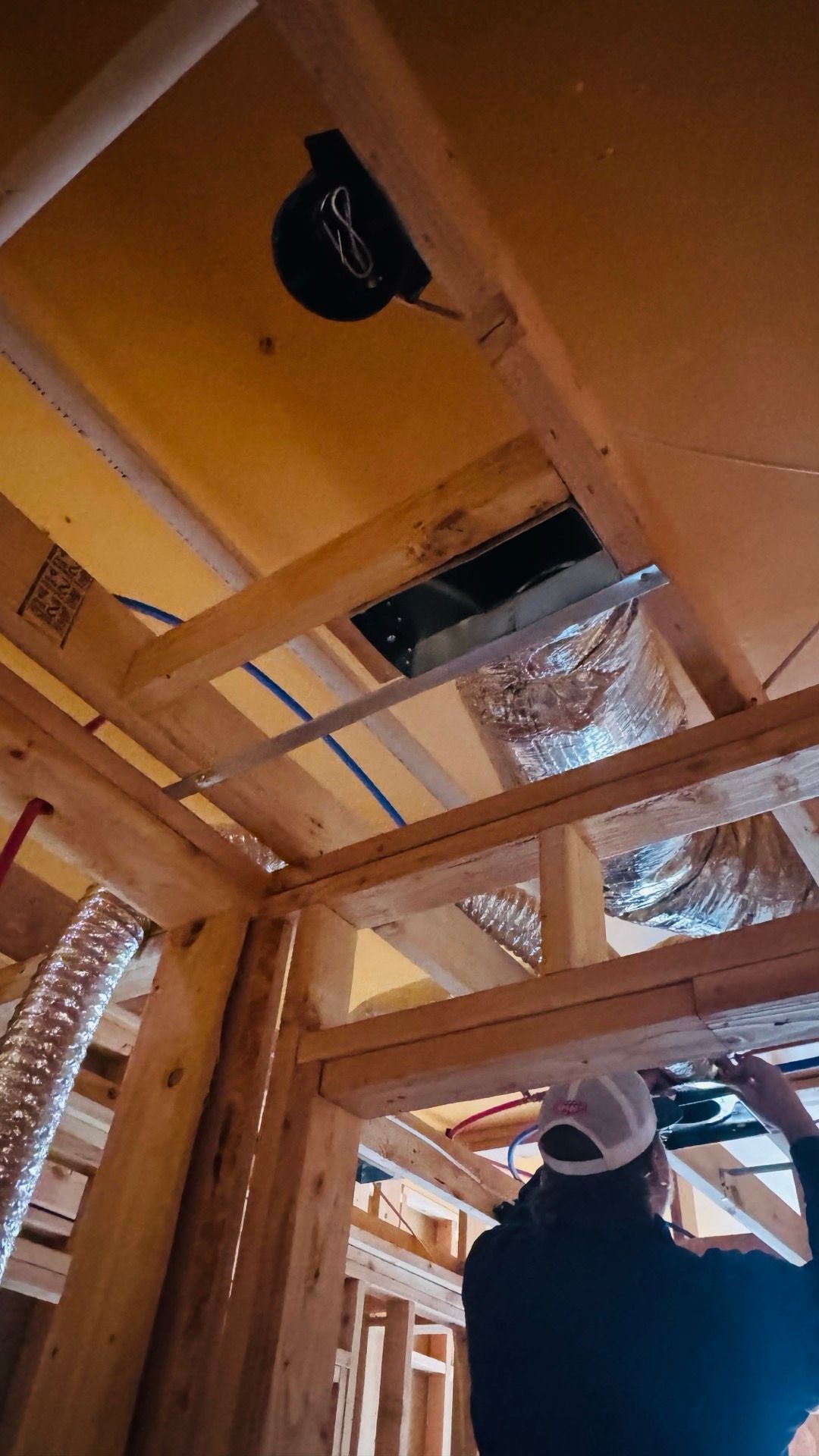 Worker installing ceiling insulation in a framed room with exposed wooden beams and insulation panels.