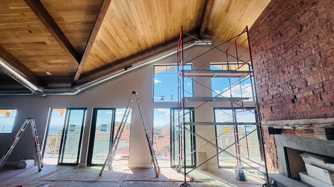 Interior under renovation with scaffolding, exposed brick fireplace, and large windows under a wood ceiling