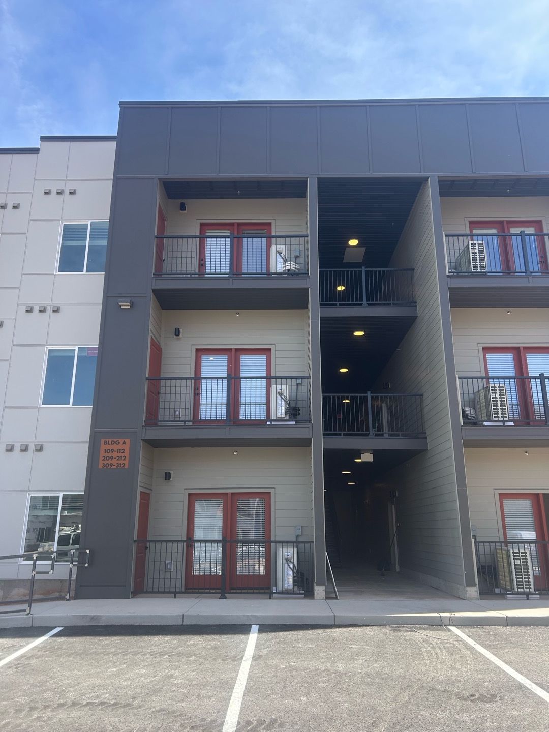 Apartment building exterior with balconies and central stairwell above a parking lot