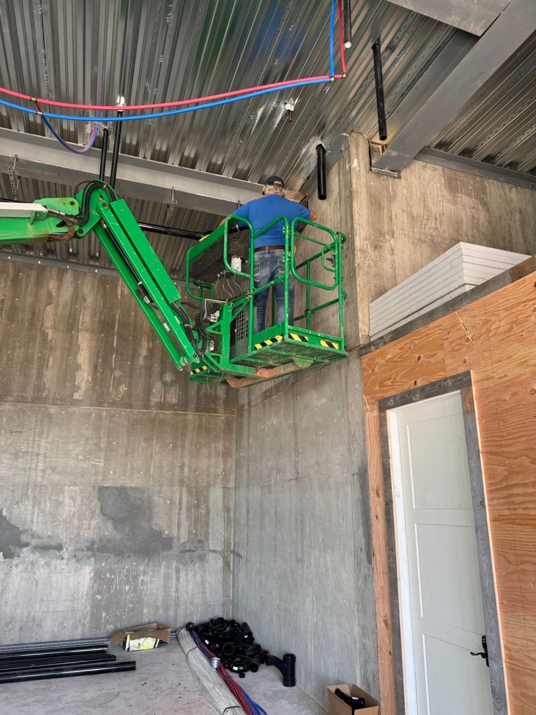 Worker on green lift repairing ceiling in unfinished concrete room