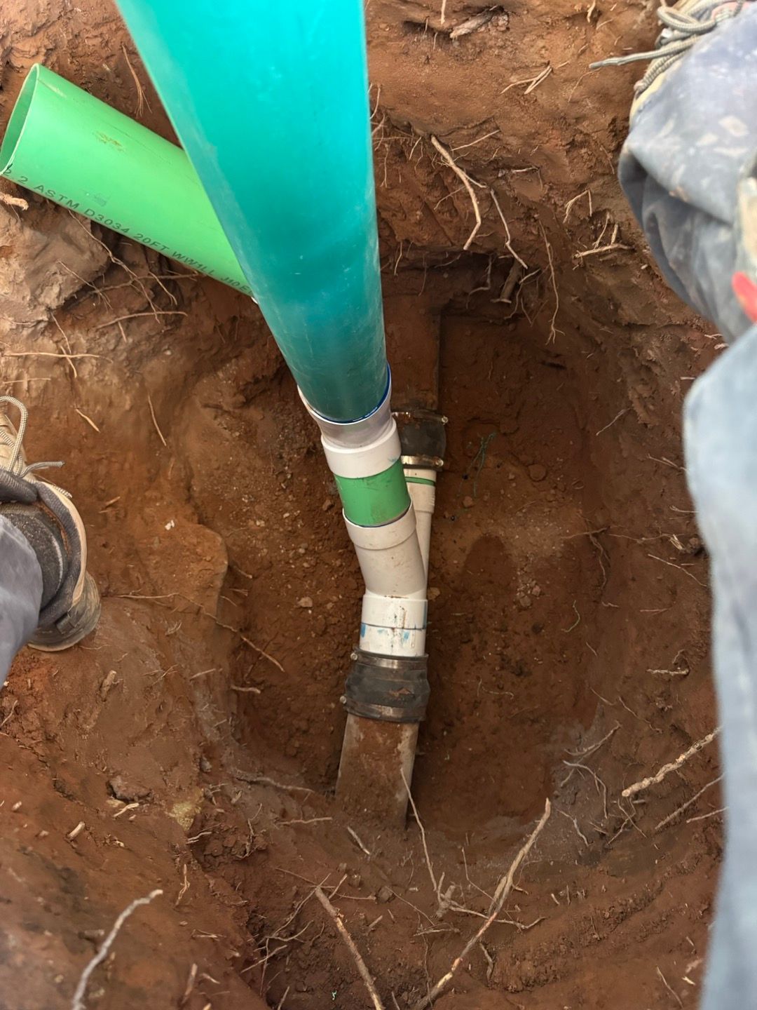 Exposed green pipe in a dirt trench with white fittings and a black connector