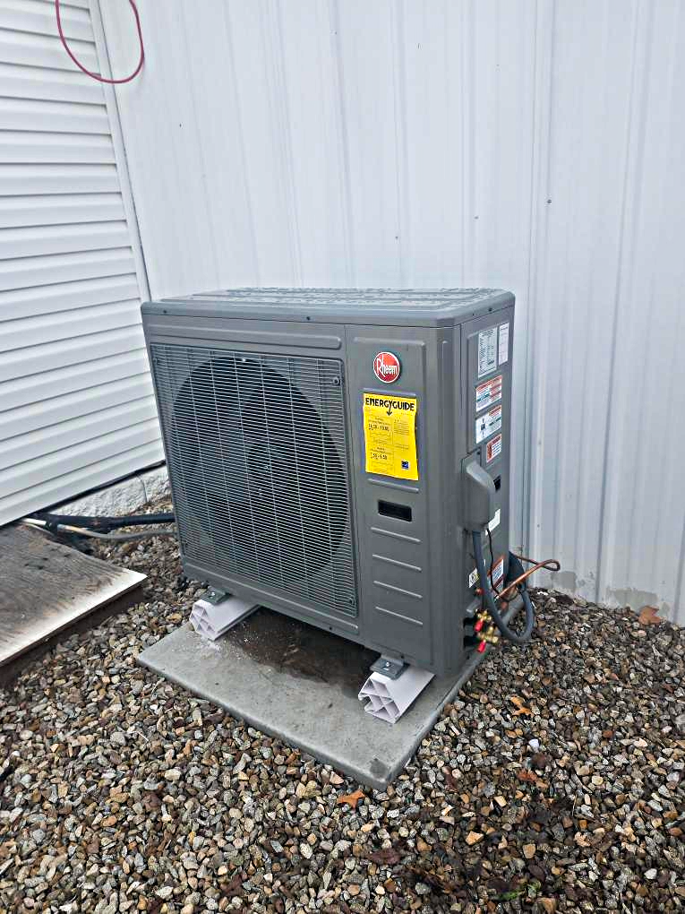 Outdoor HVAC condenser unit beside a white house wall on a gravel pad