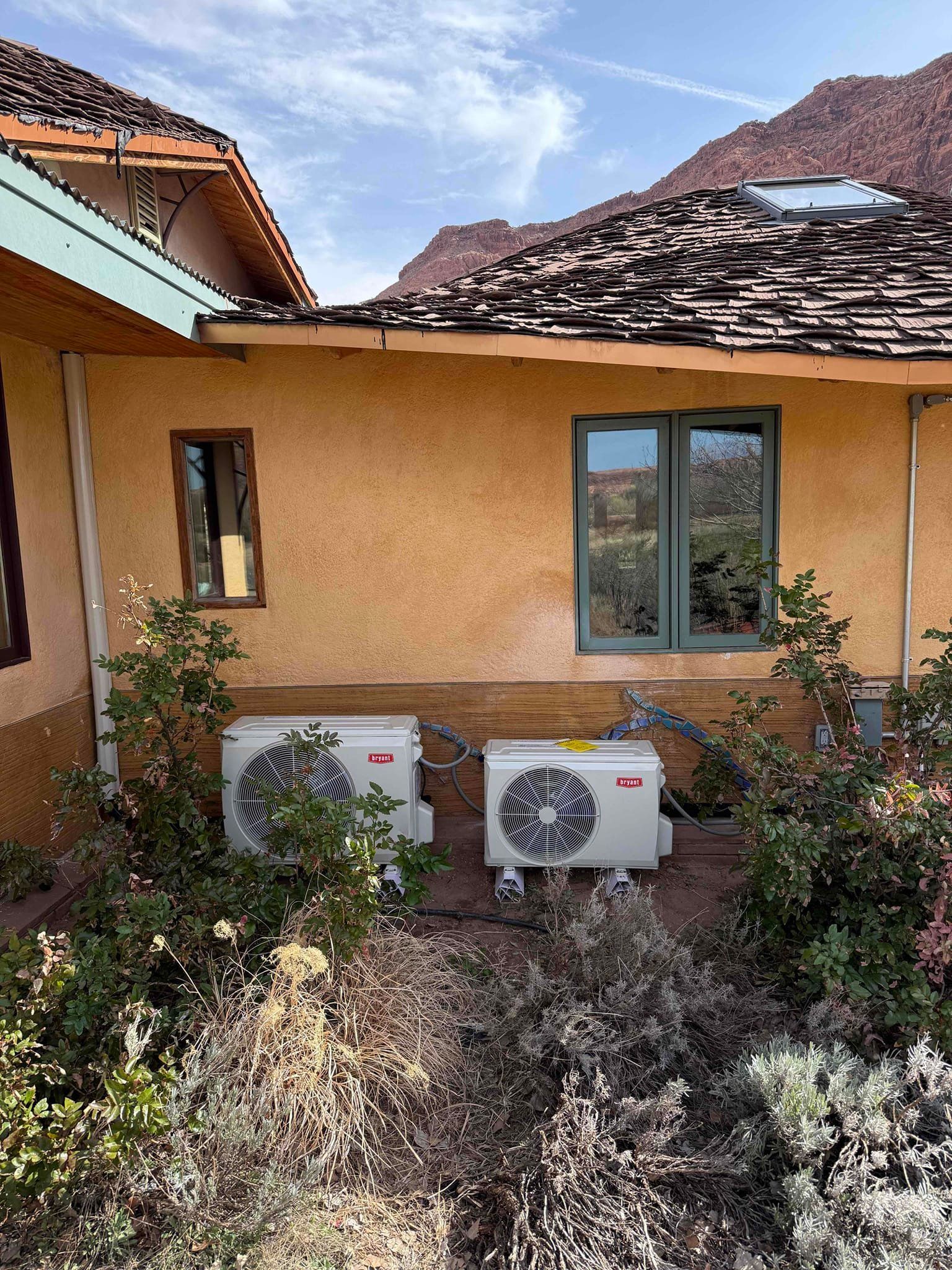 Exterior of a tan house with two air conditioning units and a mountain backdrop