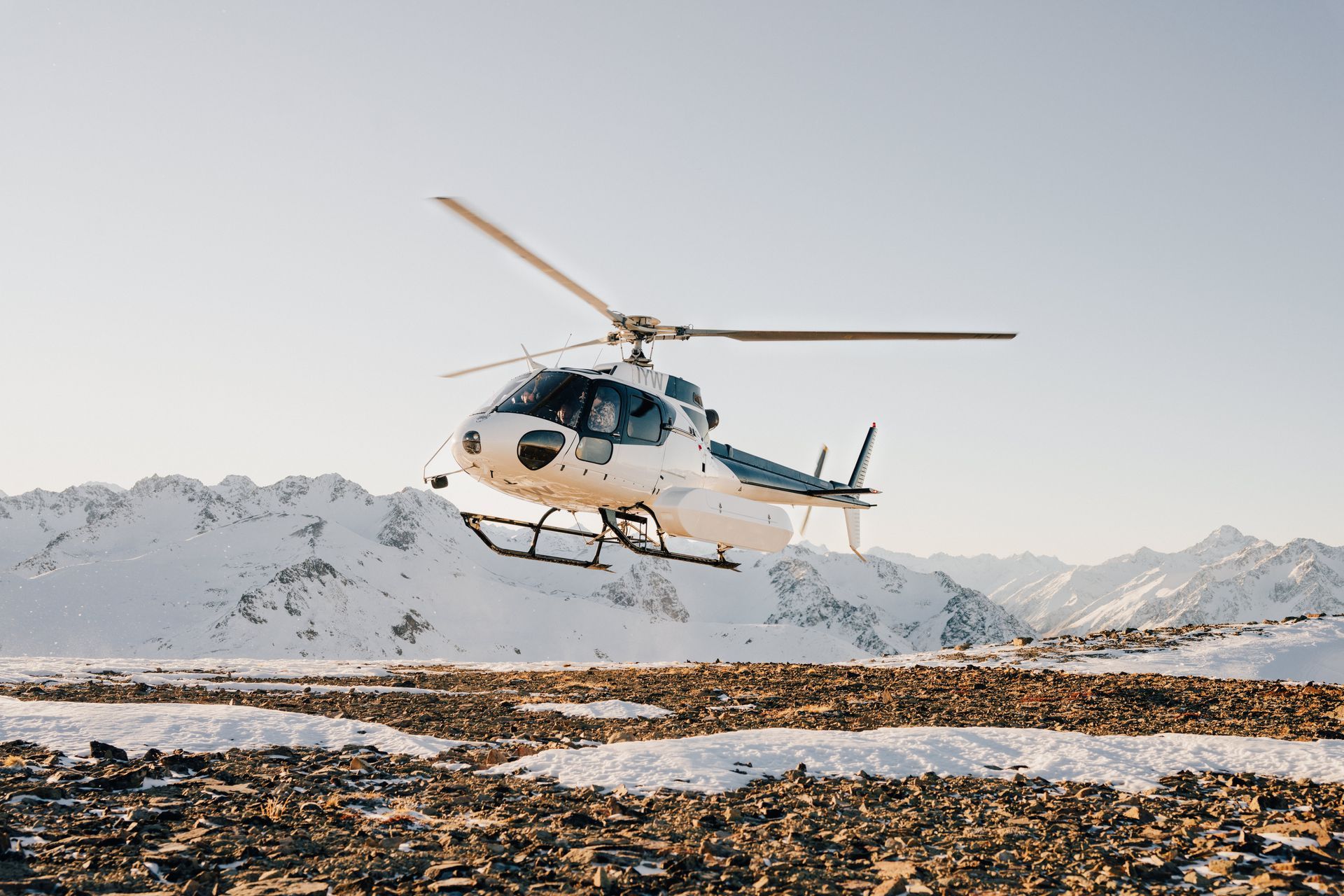 A helicopter is flying over a snowy field with mountains in the background.