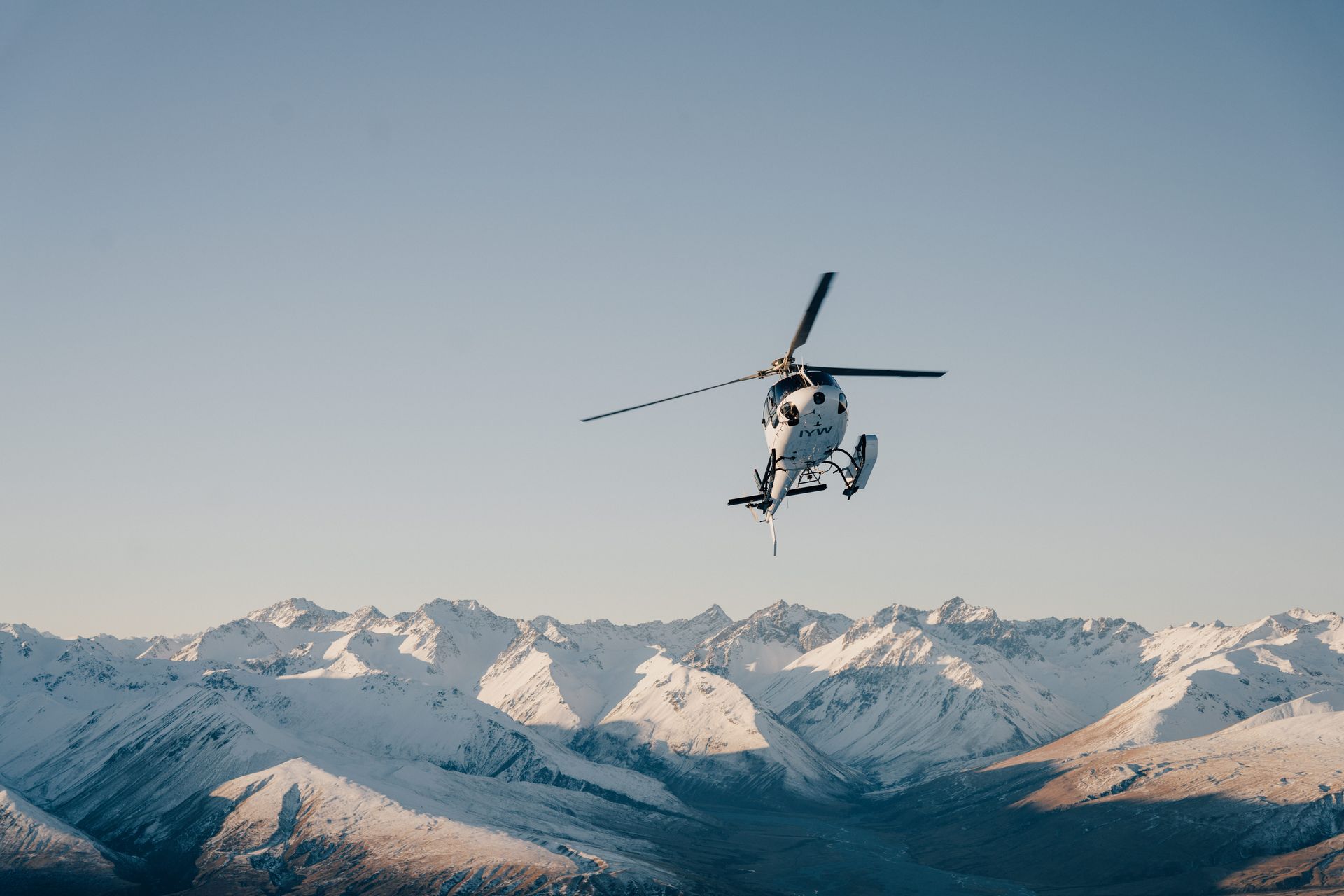 A helicopter is flying over a snowy mountain range. Rival Hunts NZ