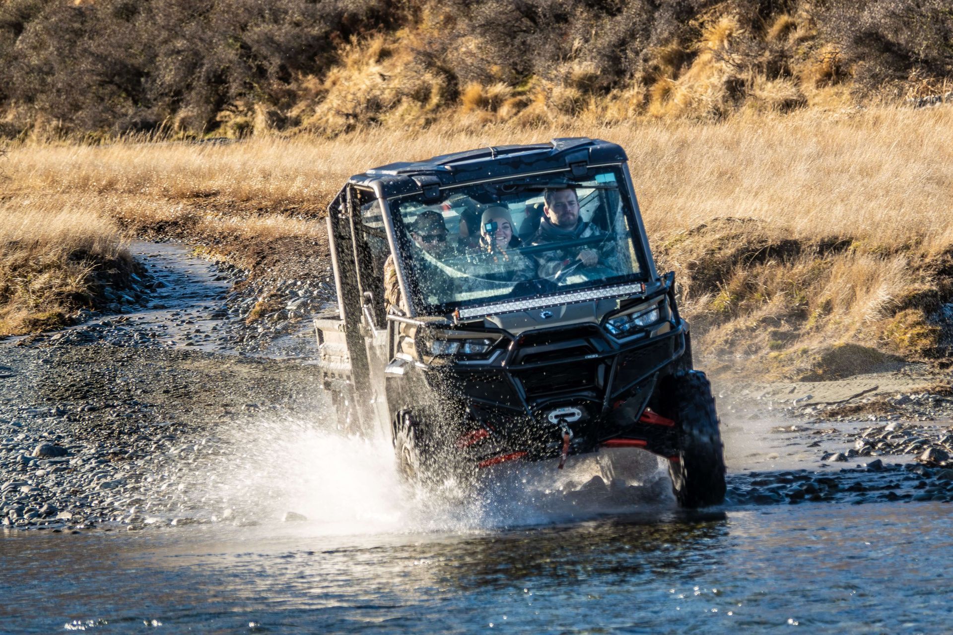 A vehicle is driving through a river on a dirt road.
