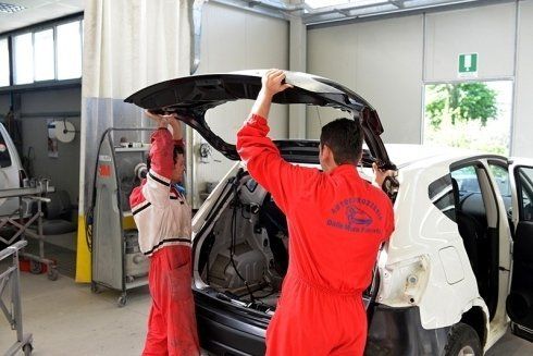 Due meccanici installano il portellone di un'auto in un'officina.