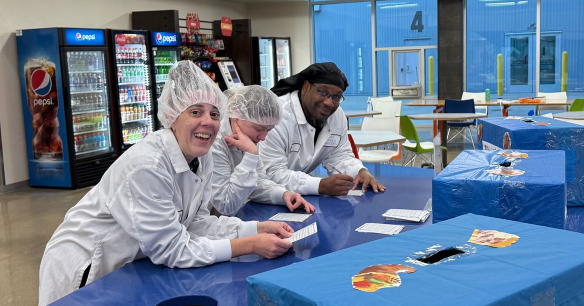 Three people in white lab coats leaning over a blue countertop.
