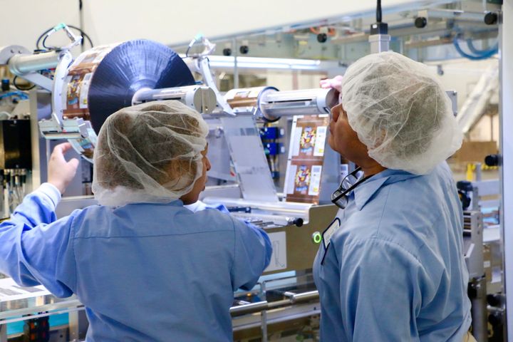 Two women in blue shirts and hairnets operating a cookie packaging line.