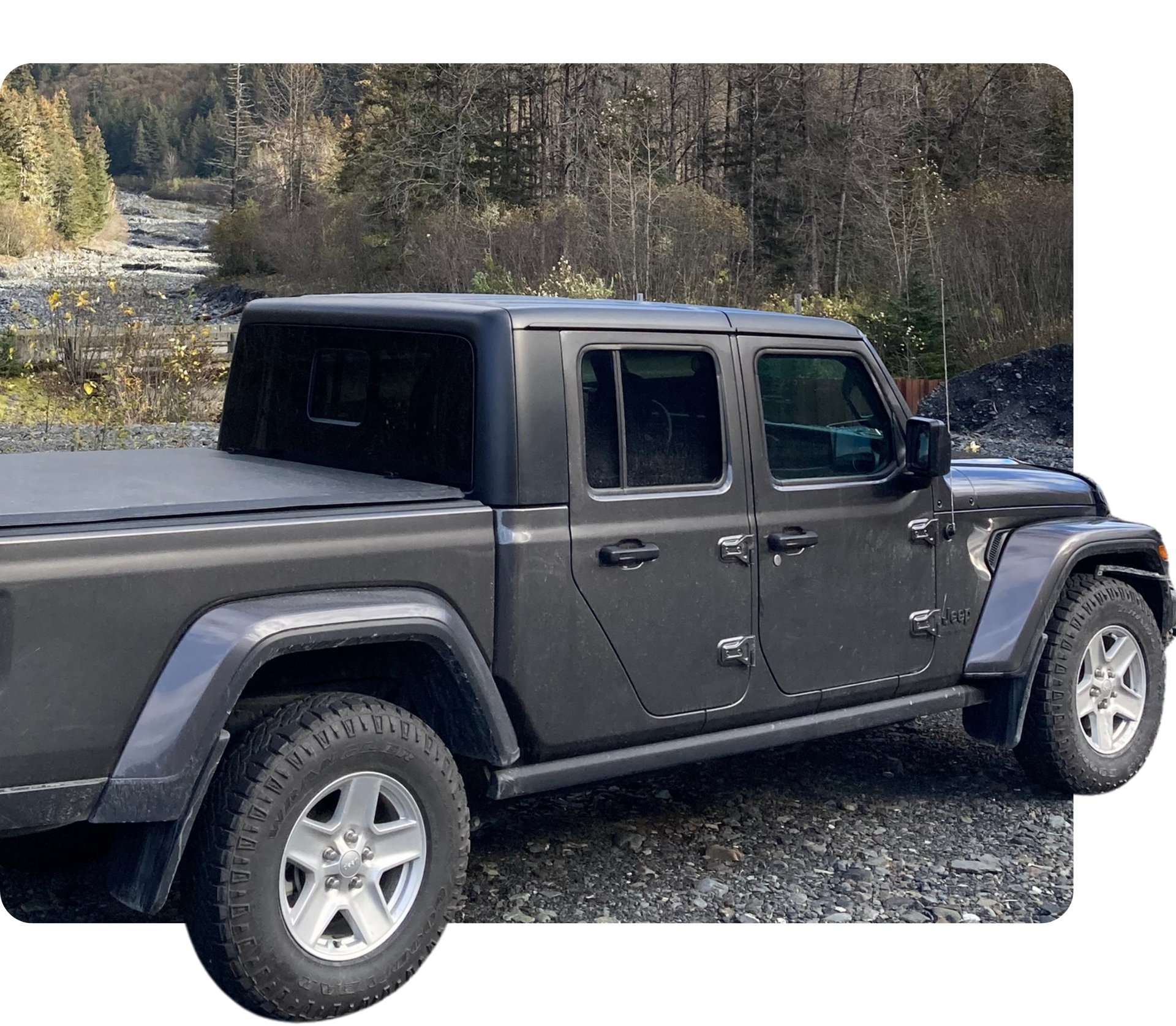 Gray pickup truck parked on gravel beside a wooded area