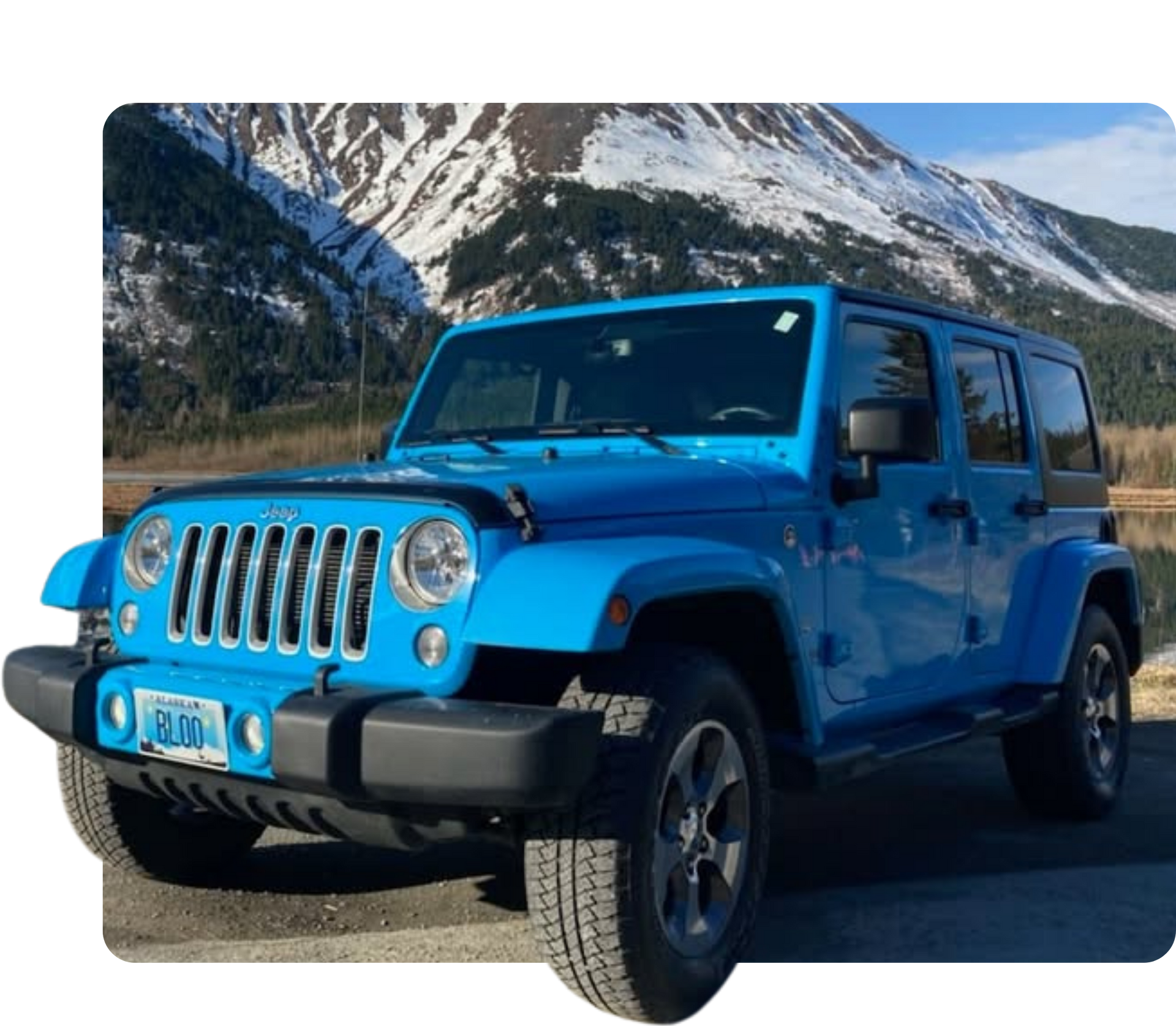 Blue Jeep Wrangler parked on a road with snowy mountains in the background