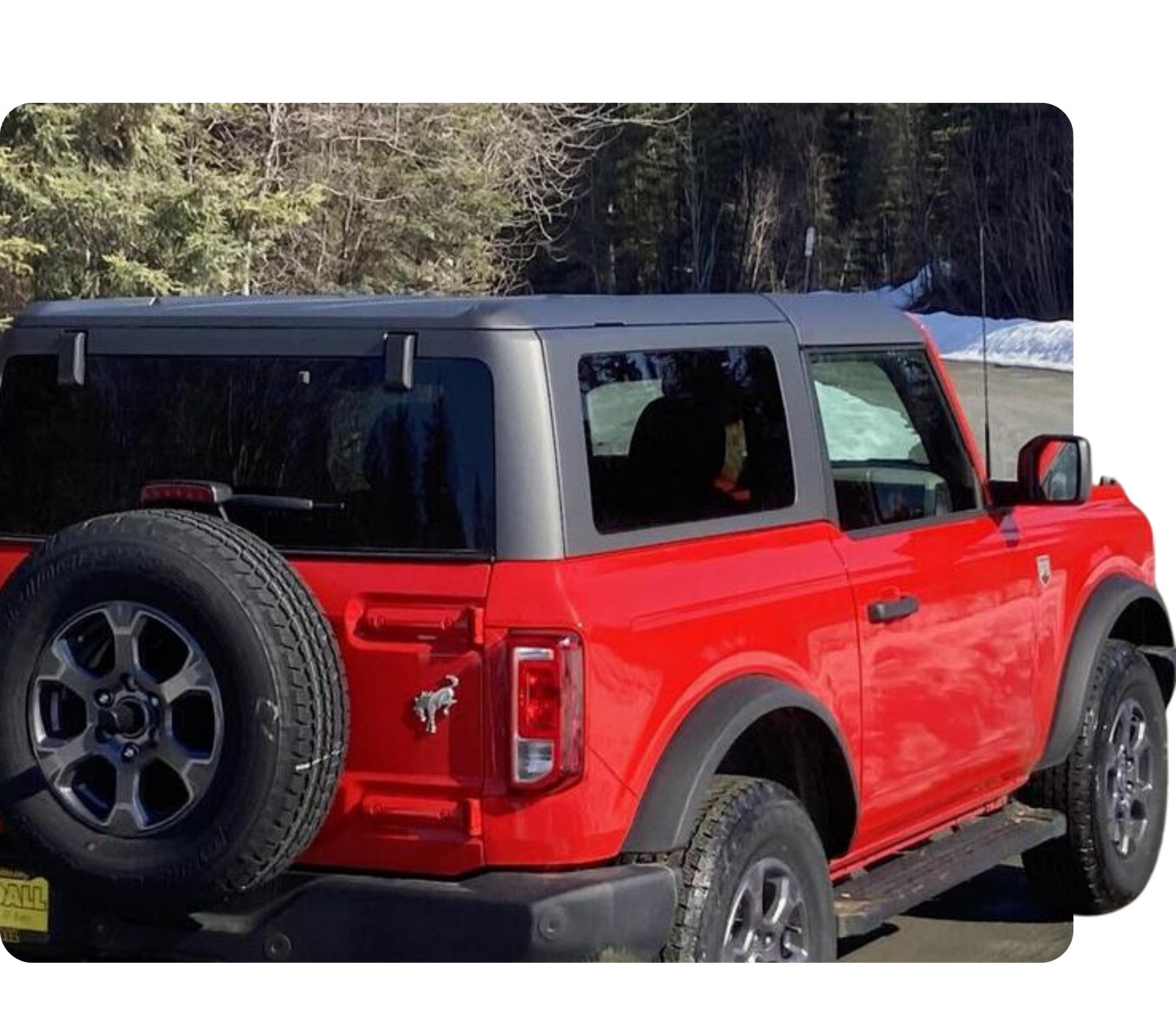 Red off-road SUV with black hardtop parked outdoors near trees and snow.