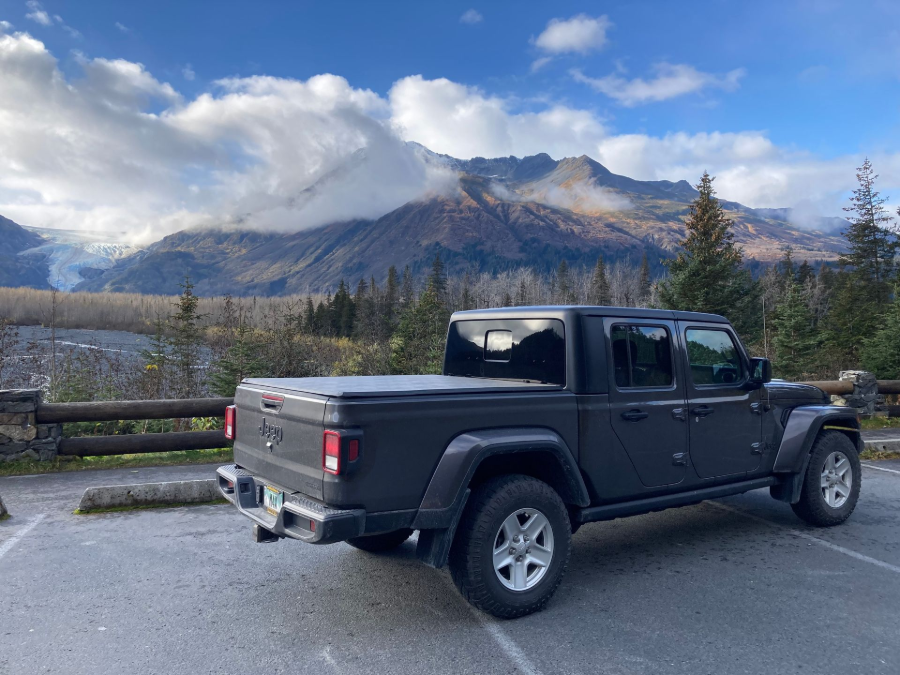 Bright blue Jeep Wrangler parked on a road with snowy mountains and a lake in the background