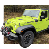 Bright lime-green Jeep Rubicon parked on grass near a wooded area
