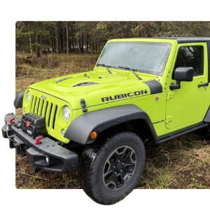 Bright lime-green Jeep Rubicon parked on grass near a wooded area