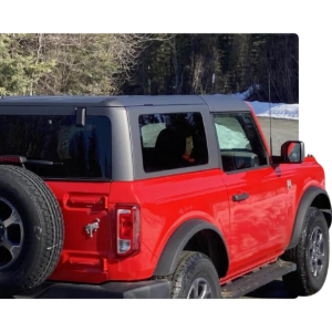 Red two-door off-road SUV with black soft top parked outdoors near snow and trees