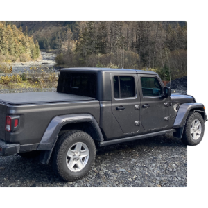 Gray pickup truck parked on a rocky path with trees and a river in the background