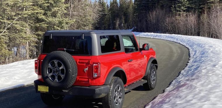 Red Jeep Wrangler parked on a snowy mountain road beside a forest