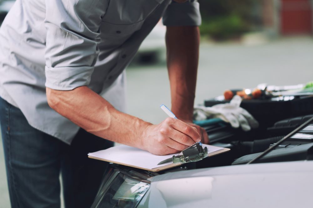A Man is Writing on a Clipboard While Looking Under the Hood of a Car — Skazas Automotive In Cardiff, NSW