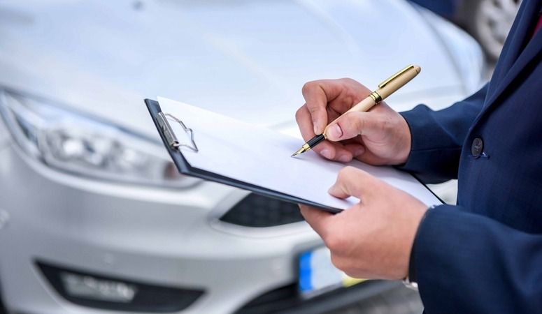 A Man is Writing on a Clipboard in Front of a Car — Skazas Automotive In Cardiff, NSW