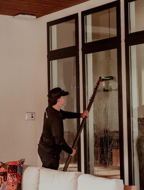 Person using a long window-cleaning tool on tall glass doors inside a room