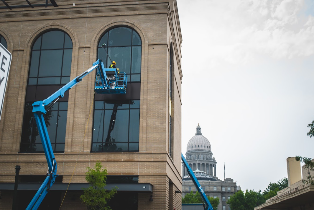 Blue lift bucket on a building facade near a domed capitol, with arched windows and trees below
