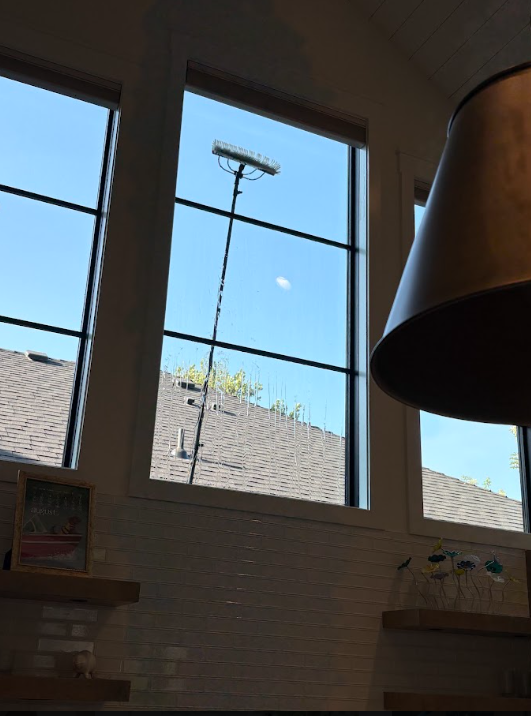 Bright blue sky seen through three windows above a brick wall, with a streetlight outside and a lamp indoors