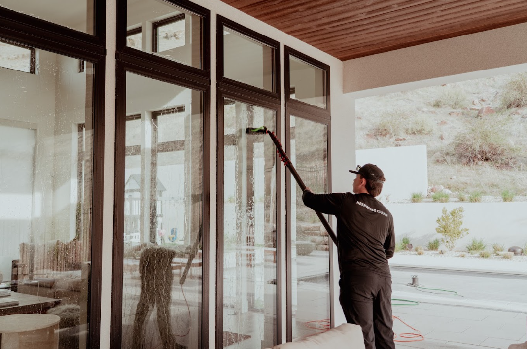 Worker washing large glass doors with a long-handled squeegee outside a modern home